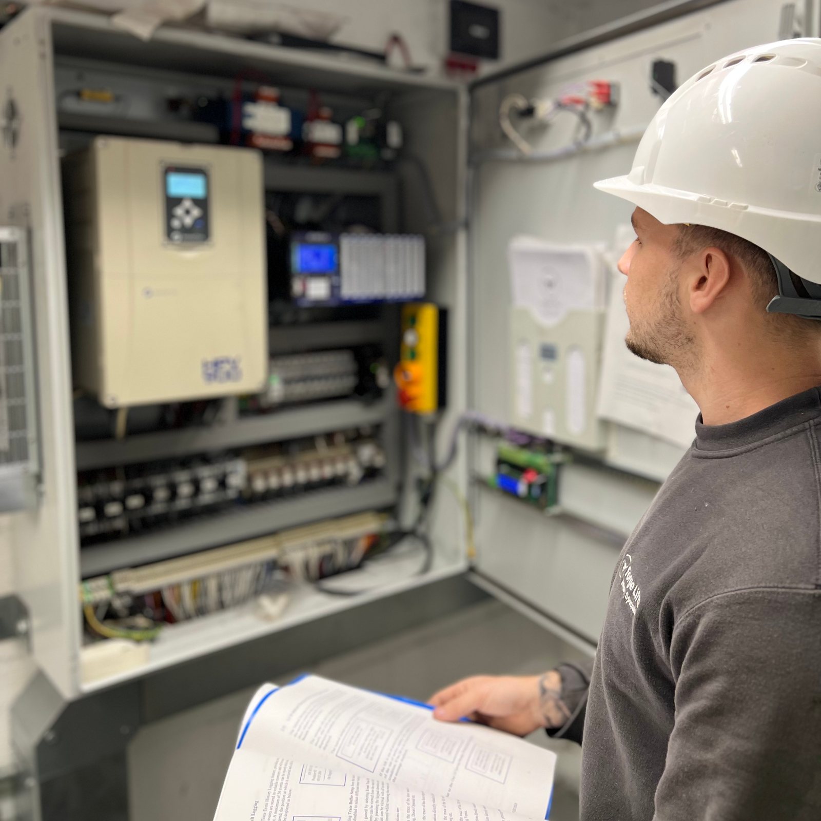 Forge Lifts engineer reviewing a lift control cabinet with technical documentation