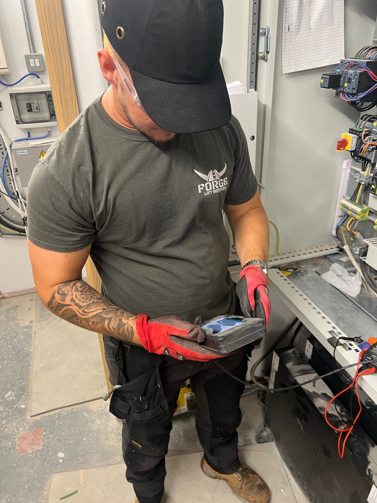 Forge Lifts engineer using a handheld diagnostic instrument beside a lift control cabinet