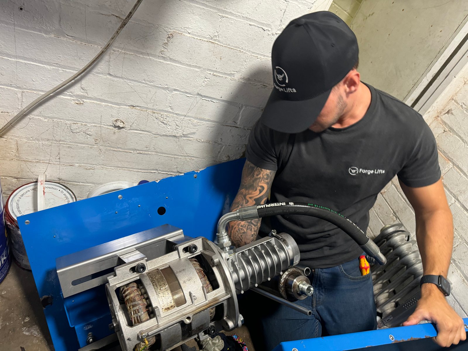 Forge Lifts engineer working on a lift motor and drive assembly in a blue frame