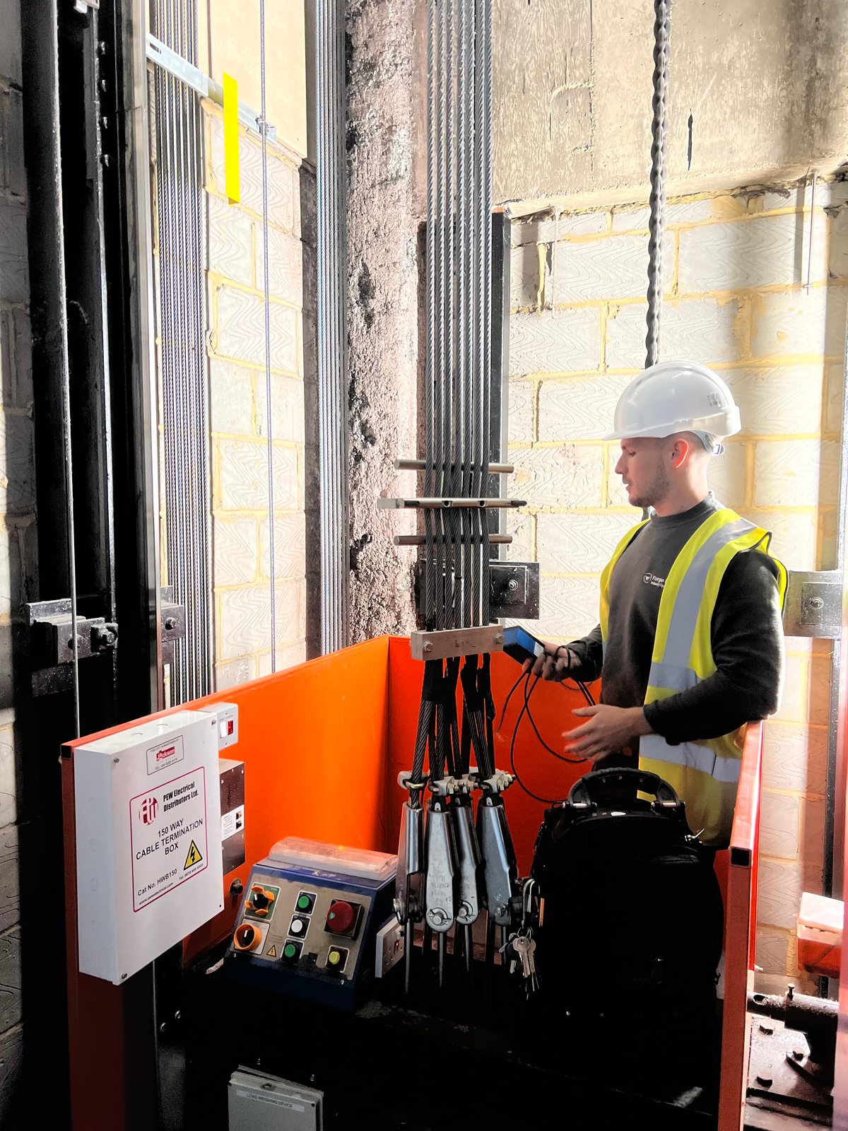 Forge Lifts engineer using handheld test equipment beside lift ropes